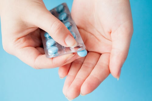Young woman pushing blue pill out of blister package